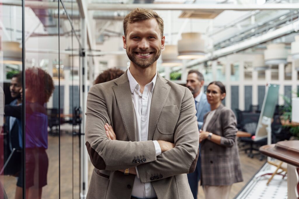 Portrait of smiling businessman standing in modern office on colleagues background